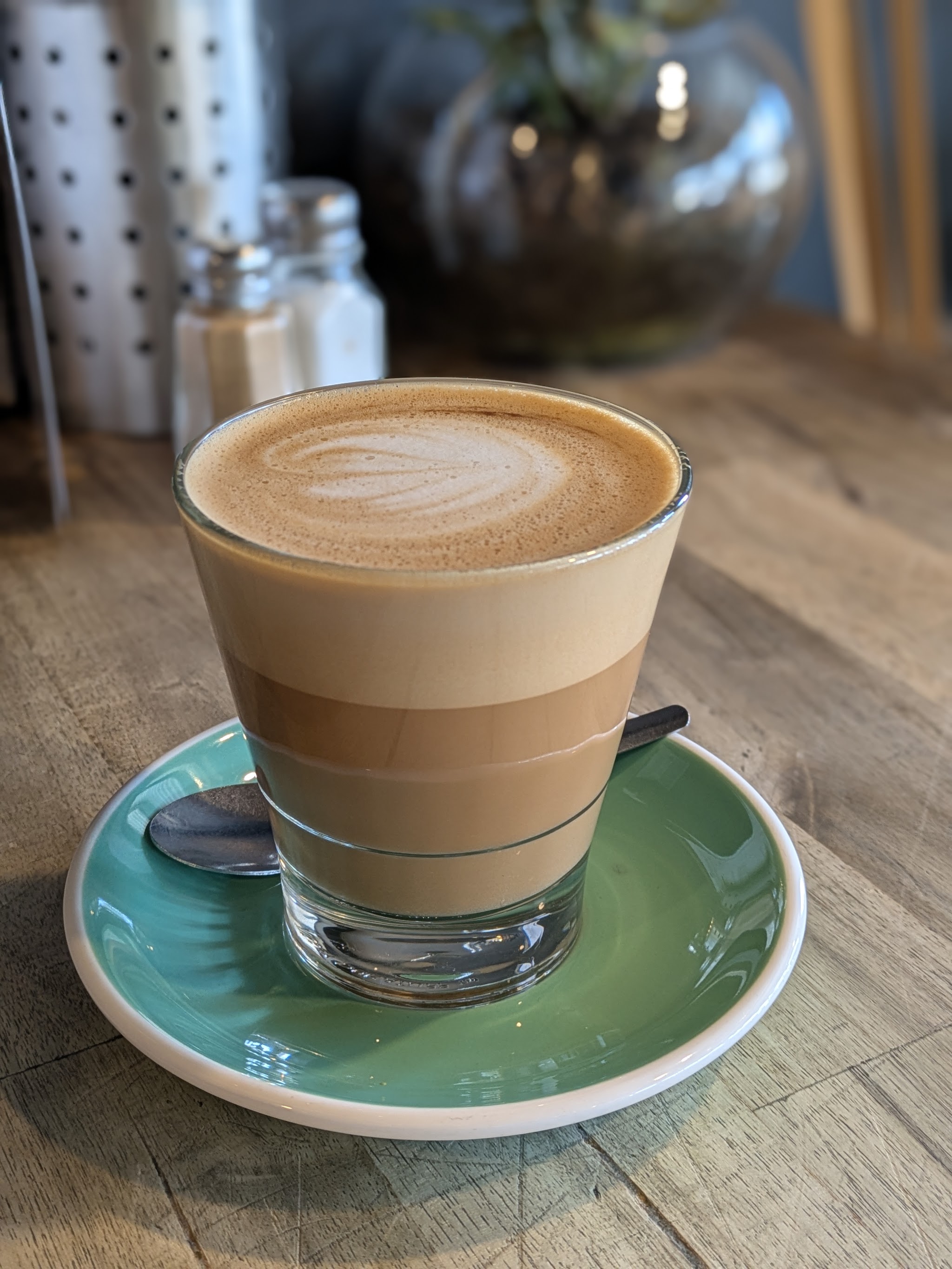 A layered latte in a glass on a green saucer